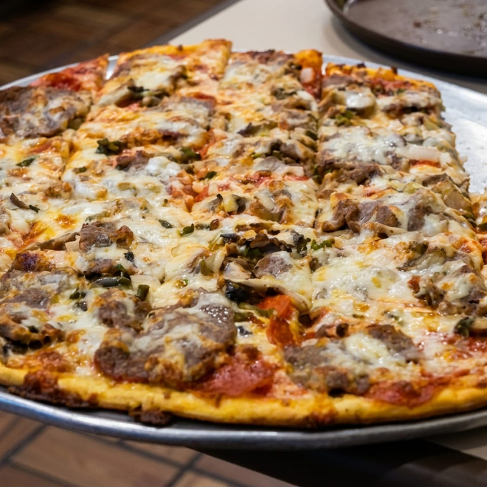 Large thin-crust pizza topped with melted cheese, mushrooms, sausage, pepperoni, and green peppers on a metal serving tray.