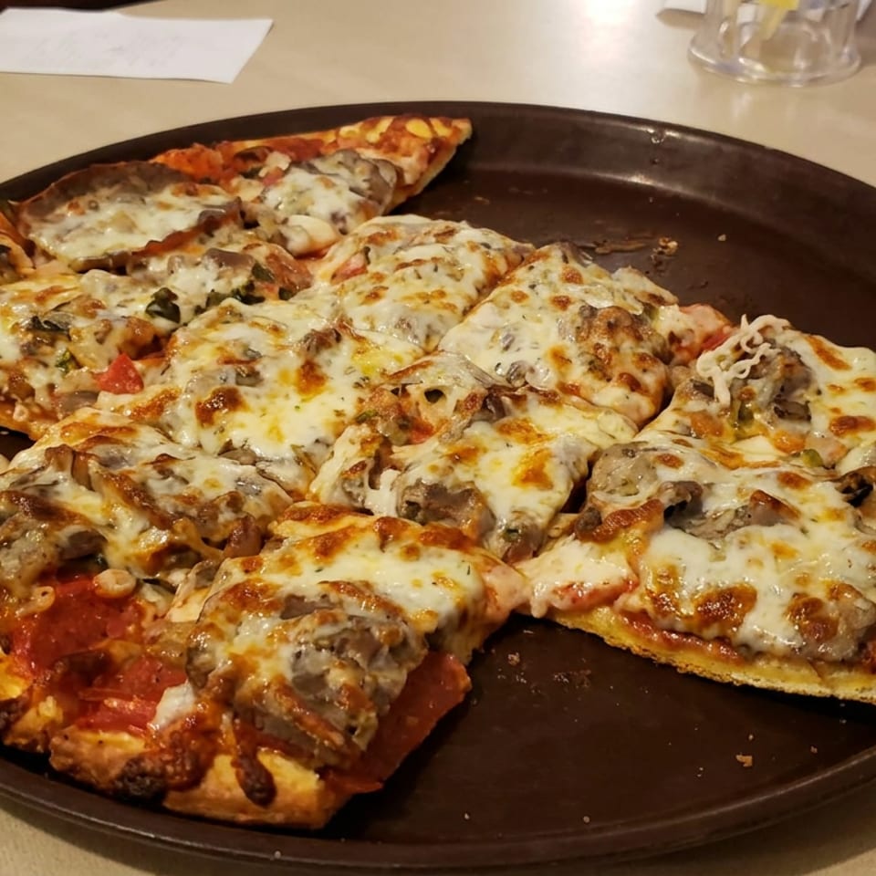 Rectangular slices of cheesy mushroom pizza arranged on a large brown platter at a restaurant table.