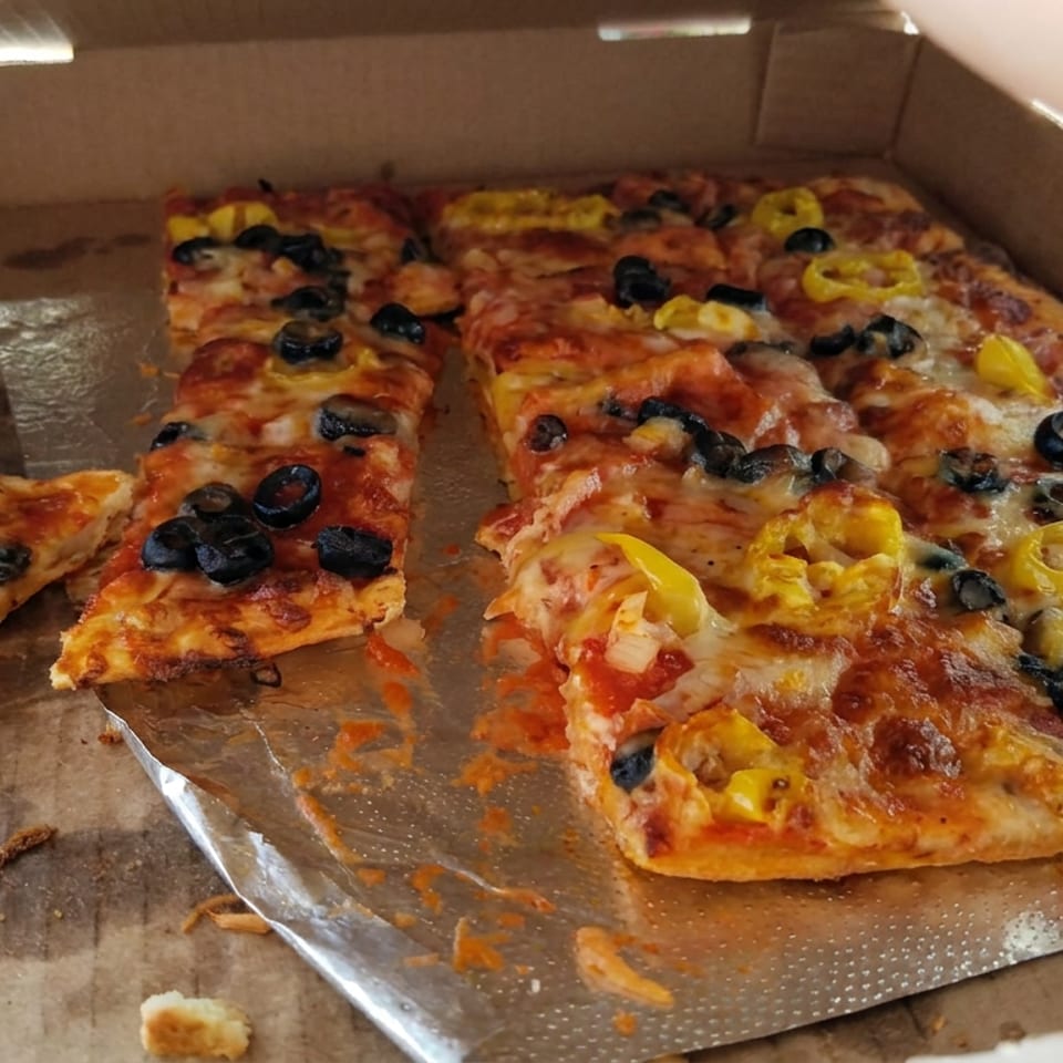 Open pizza box holding rectangular slices topped with melted cheese, black olives, and yellow peppers.